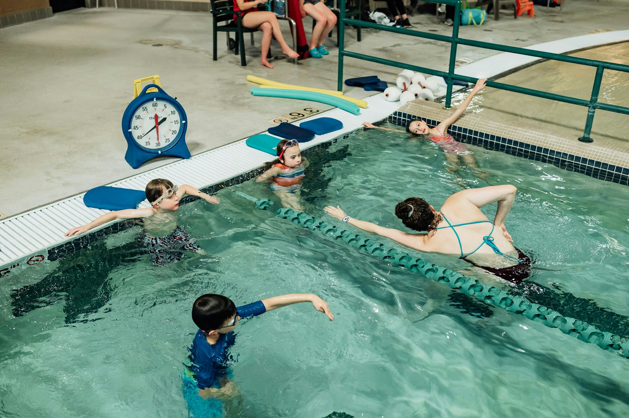 Children taking a swimming lesson with an instructor in an indoor pool.