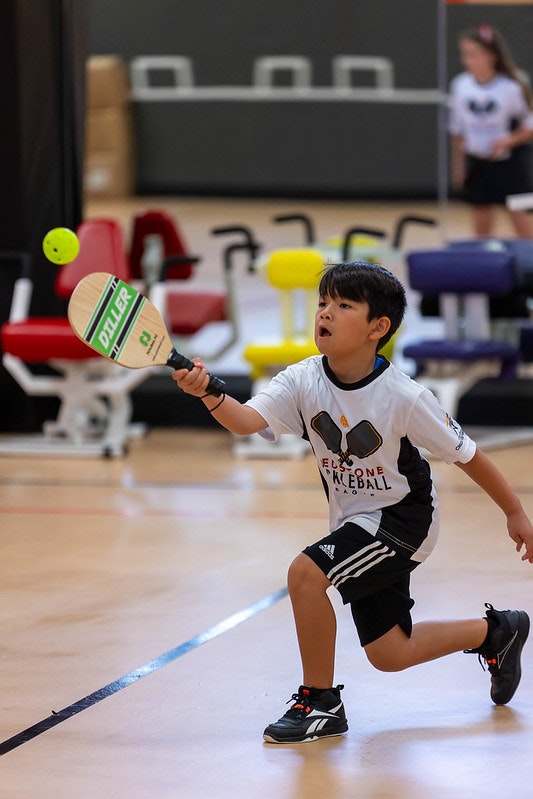 Young boy playing pickleball indoors, about to hit a ball with a paddle.