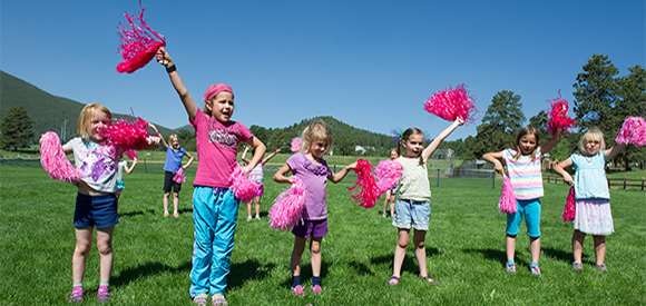 Children with pink pom-poms practicing cheerleading outdoors.