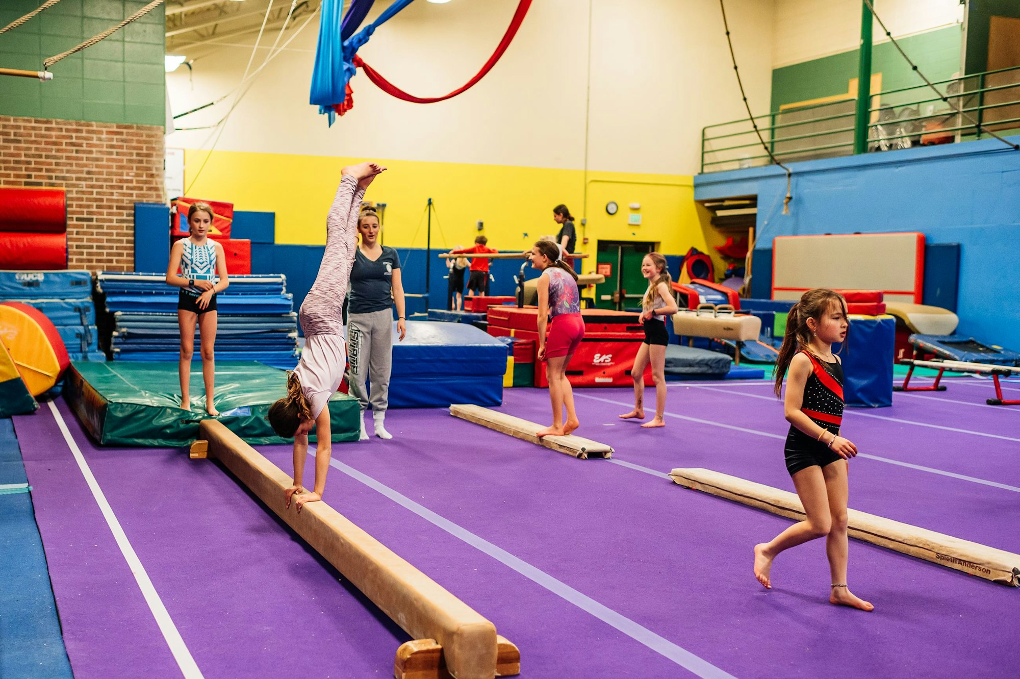 Children practicing gymnastics with an instructor in a colorful gym.