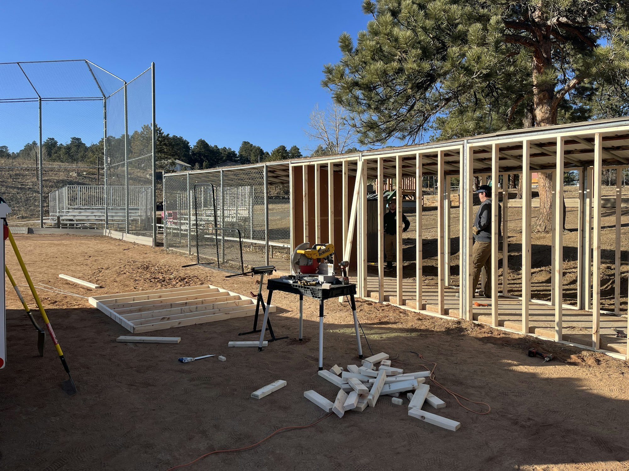Construction site with wooden framing, tools, and workers next to a fenced area.
