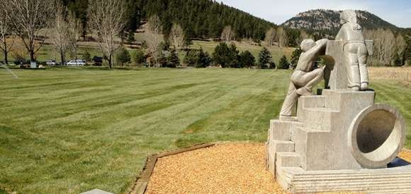 A sculpture in a grassy field with trees and hills in the background.