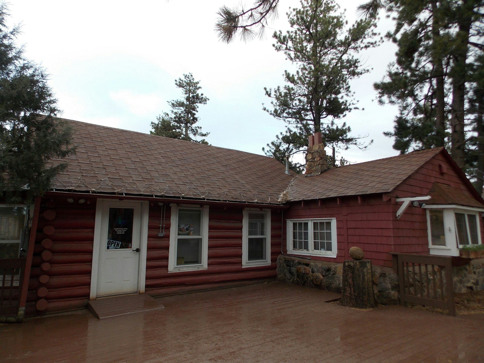 A red log cabin with a white door, security camera, and a wet pavement under a cloudy sky.