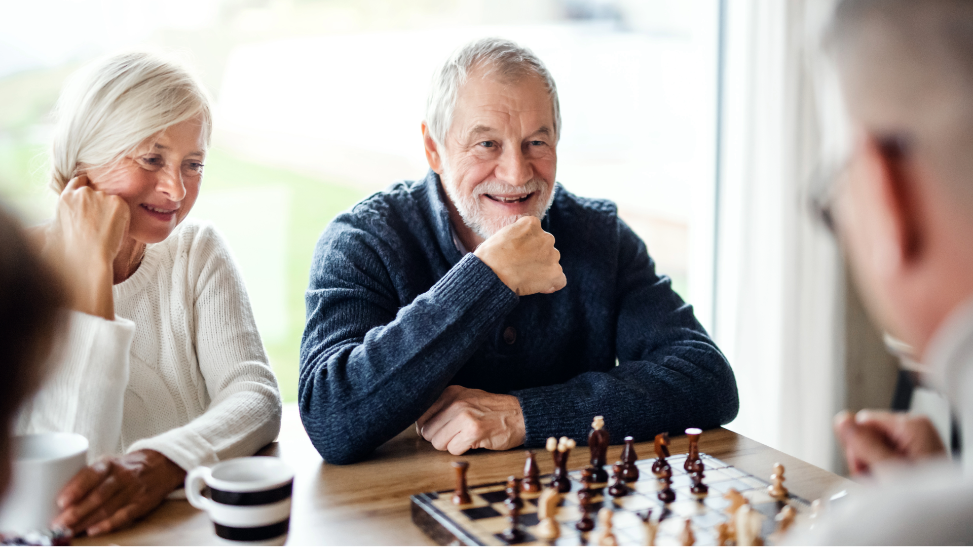 Two people smiling at a chess game, seated at a table with coffee cups.