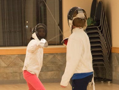 Two people fencing in a room, wearing protective gear and masks.