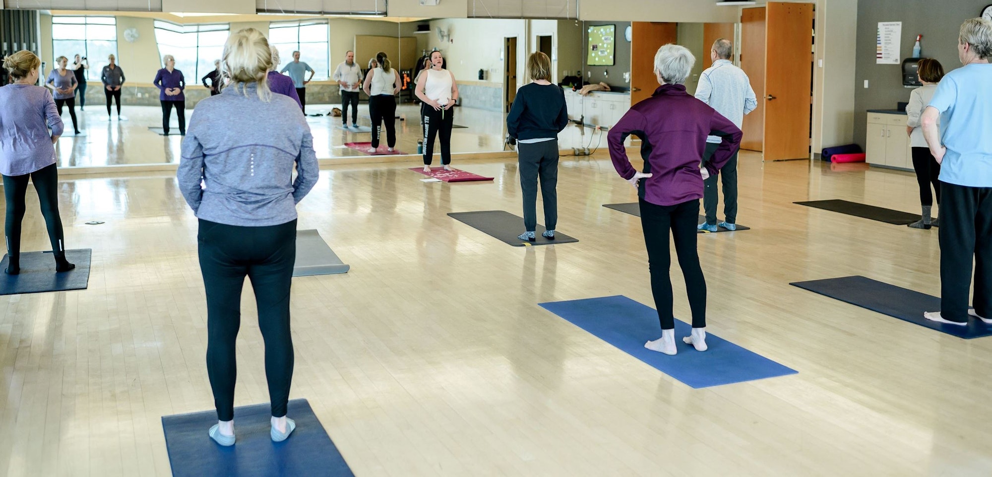 A group of people participating in an exercise or yoga class indoors, standing on mats.