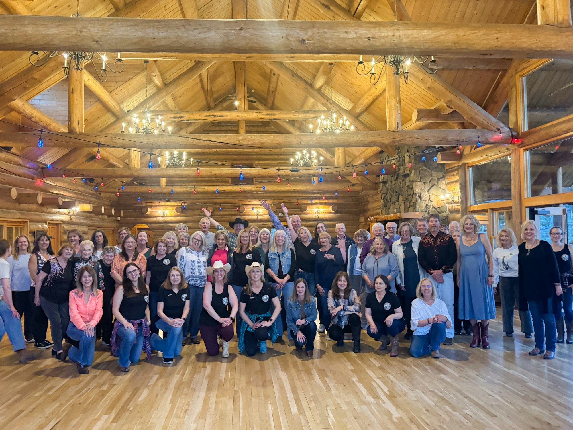 A large group of people gathered indoors, smiling, with a rustic wooden setting and festive lighting.
