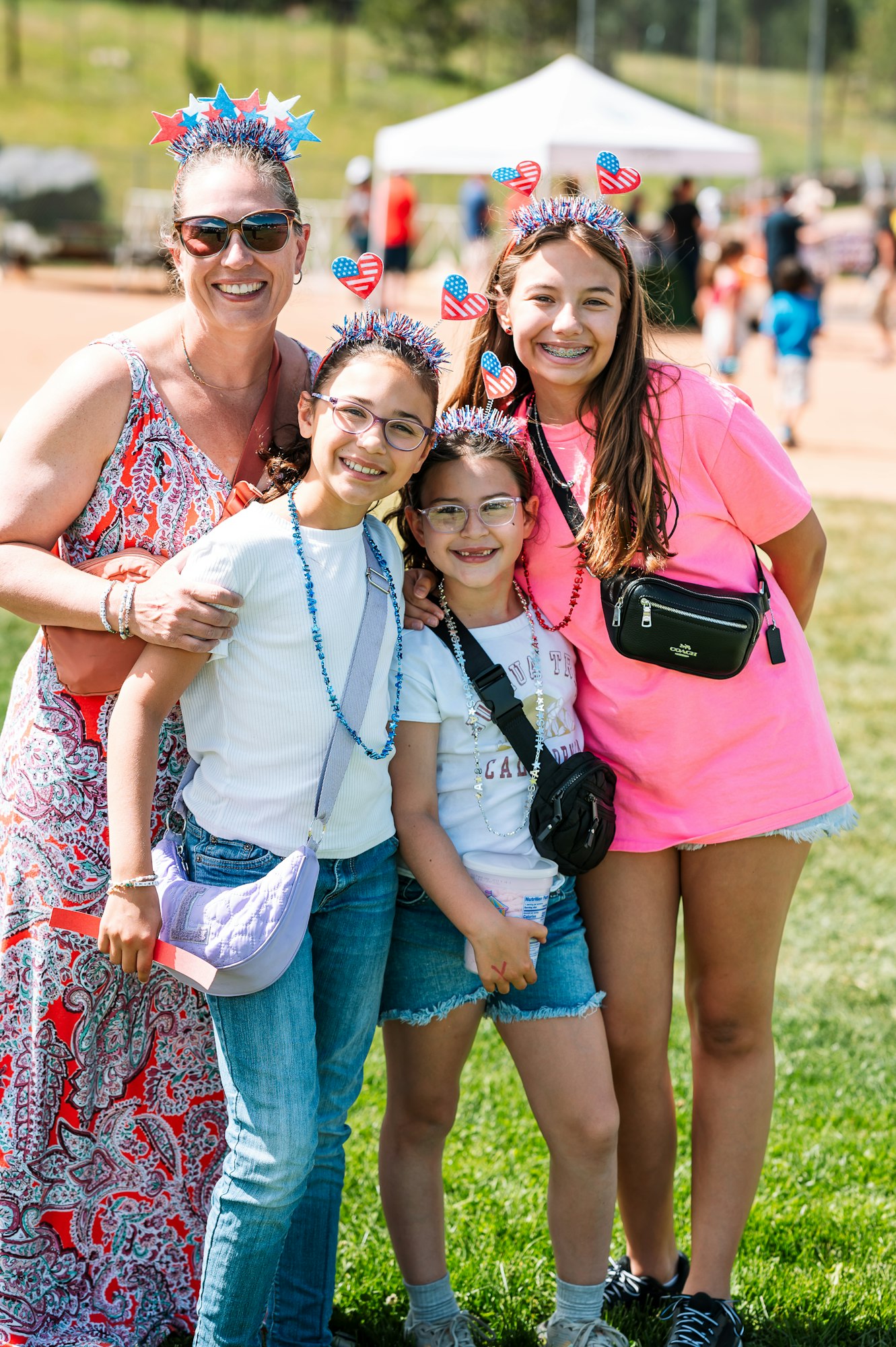 A group of four people with festive headbands, smiling outdoors at a park event.