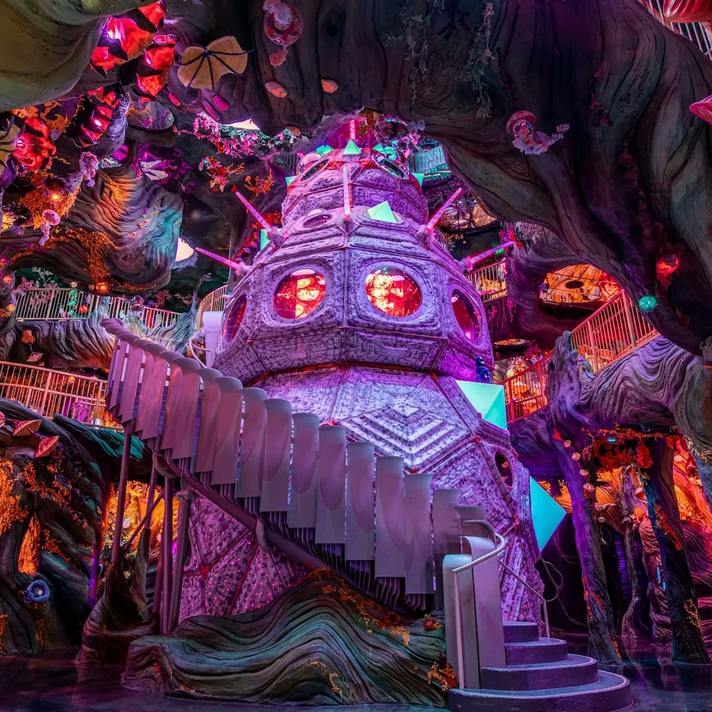 A fantastical, colorful interior featuring a spiral staircase and a unique tower-like structure illuminated by vibrant lights.