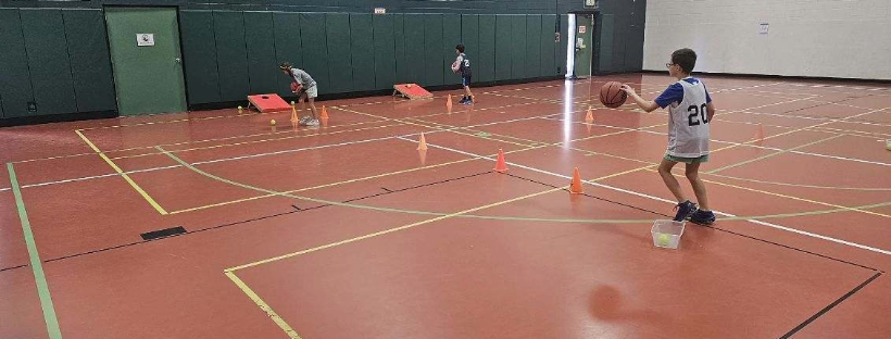 Kids practicing basketball skills in a gym with cones and boards.