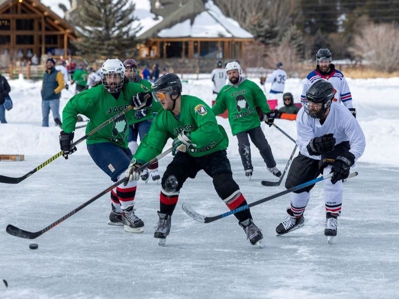 An outdoor ice hockey game with players in green and white jerseys competing on a frozen surface.
