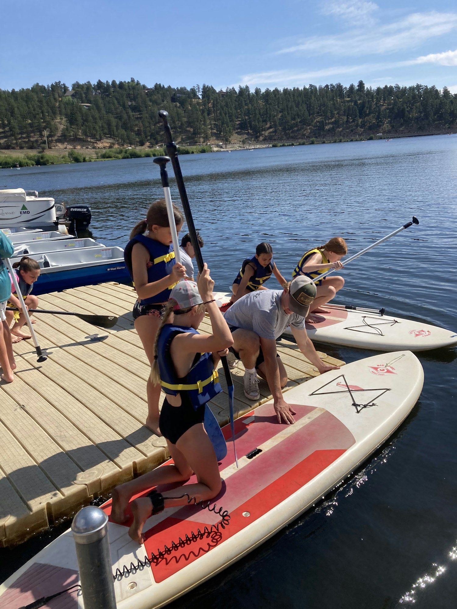 Group of people in life vests getting ready to paddleboard on a lake.