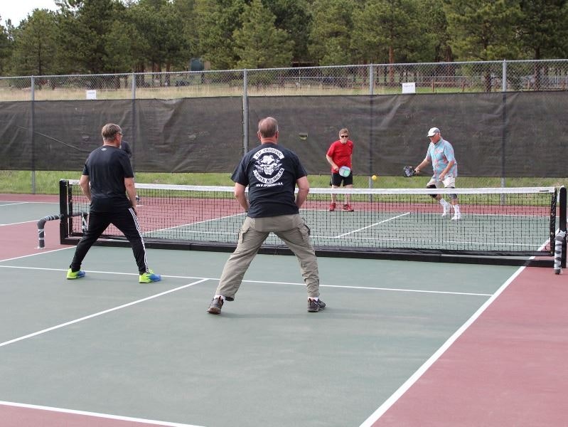 Four people playing doubles pickleball on an outdoor court.
