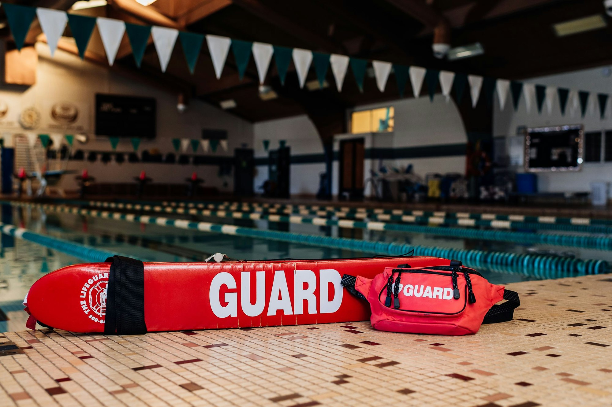 Lifesaving gear with "GUARD" text by an indoor pool with lanes and bunting decorations.