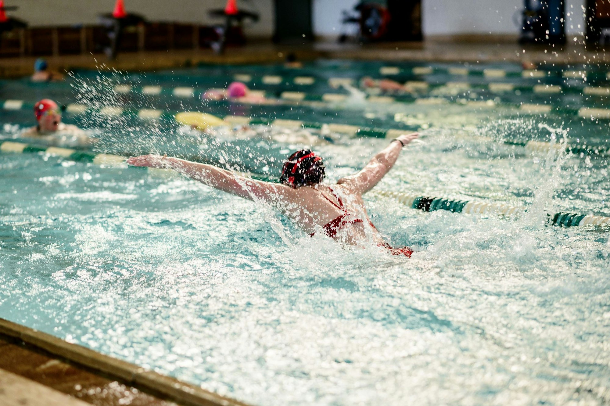 A swimmer doing the butterfly stroke in a pool with others swimming in the background.