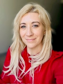 The image features a woman with long blonde hair wearing a red top, smiling at the camera. The background appears softly lit.