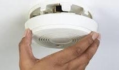 A hand holding a white smoke detector, likely being removed from its mounting.