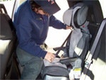 A person is installing a car seat in a vehicle, focusing on securing it properly for safety.
