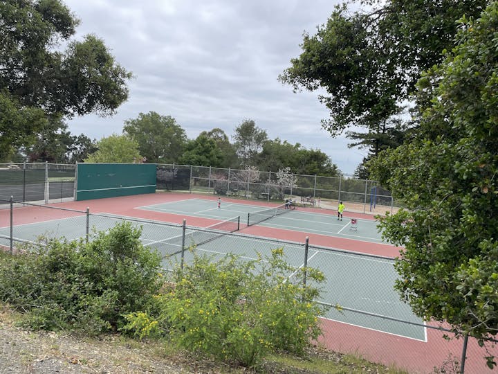 Tennis courts surrounded by trees, with people playing tennis.