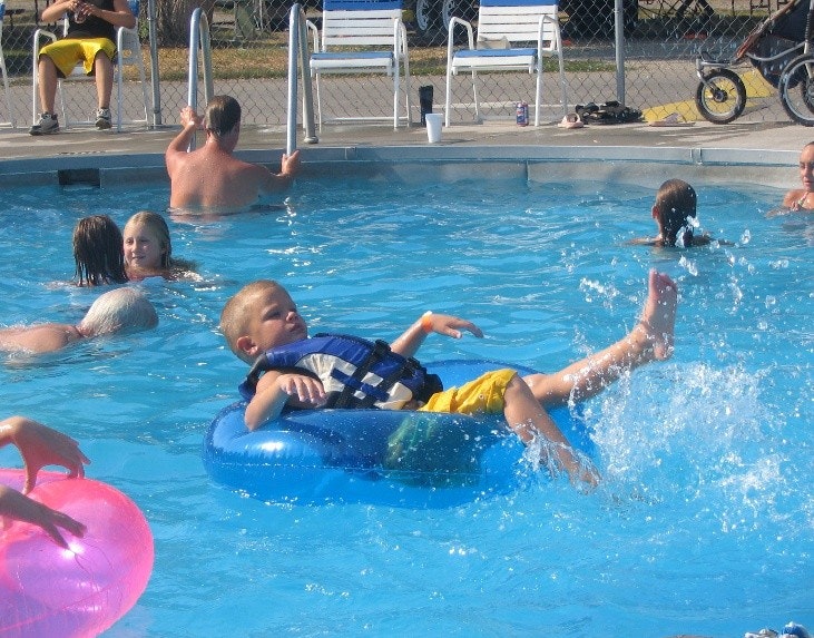 Children are playing and relaxing in a swimming pool, with some using inflatable rings.