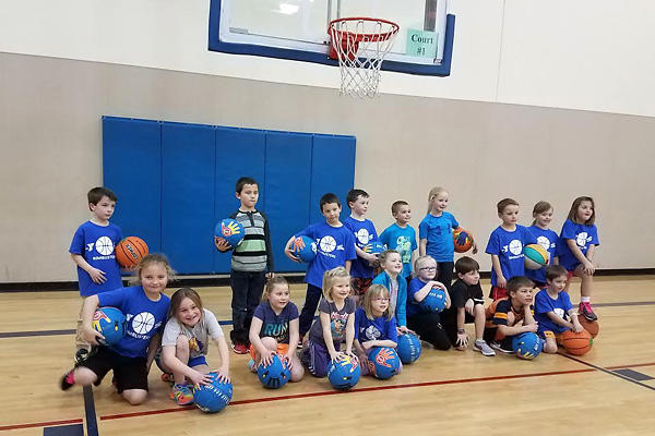 Photo of a group of kids posing with basketballs in a gymnasium