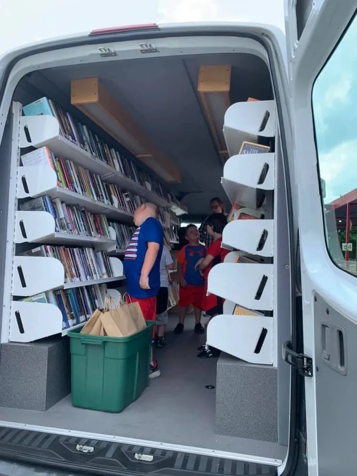 A library on wheels with shelves of books and people browsing inside a vehicle.