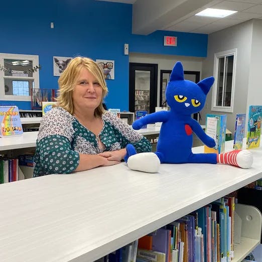 A woman and a blue plush toy on a library counter.