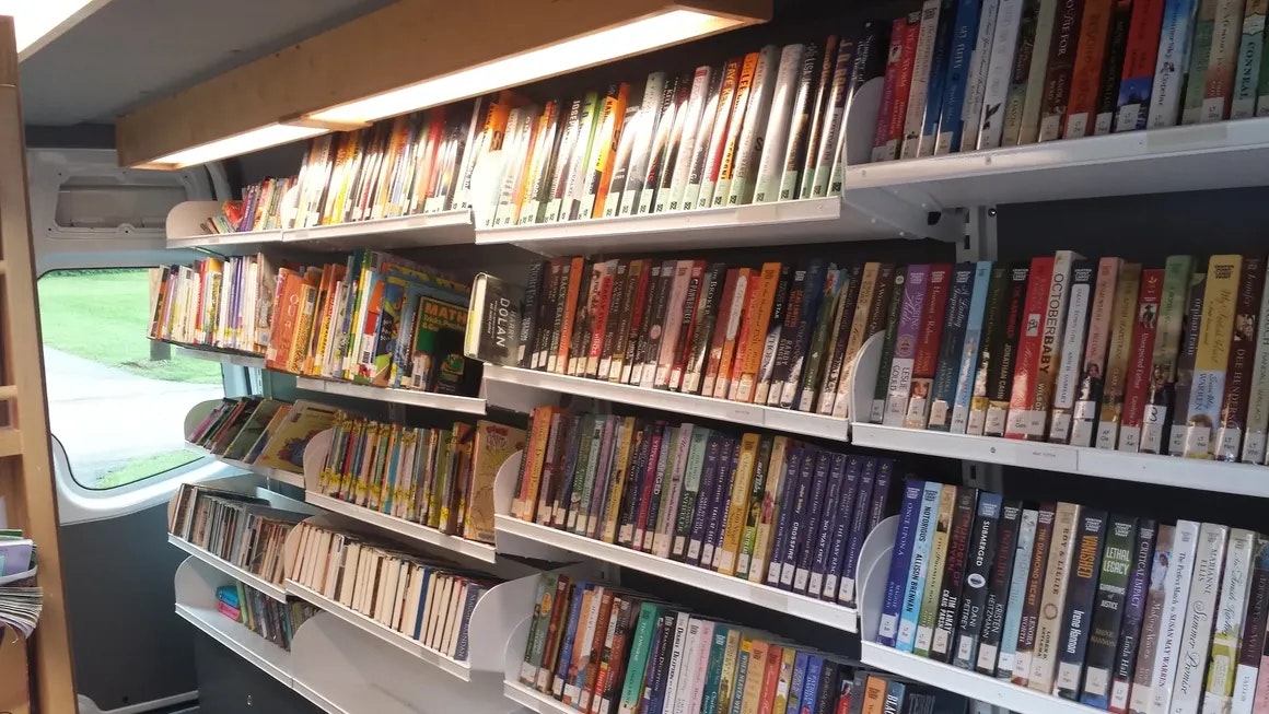 A bookshelf with various books, a window on the side in a cozy room or vehicle.