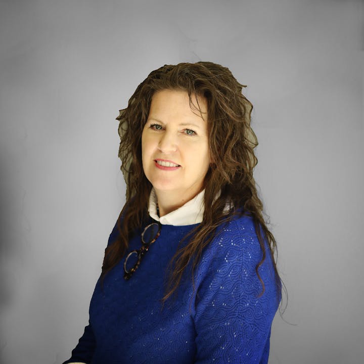 A person wearing a blue top and white collar, with eyeglasses hanging on the front.