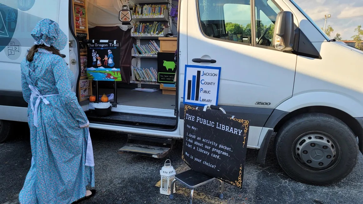 A person in historical dress looks at a mobile library van with a sign: "Jackson County Public Library."