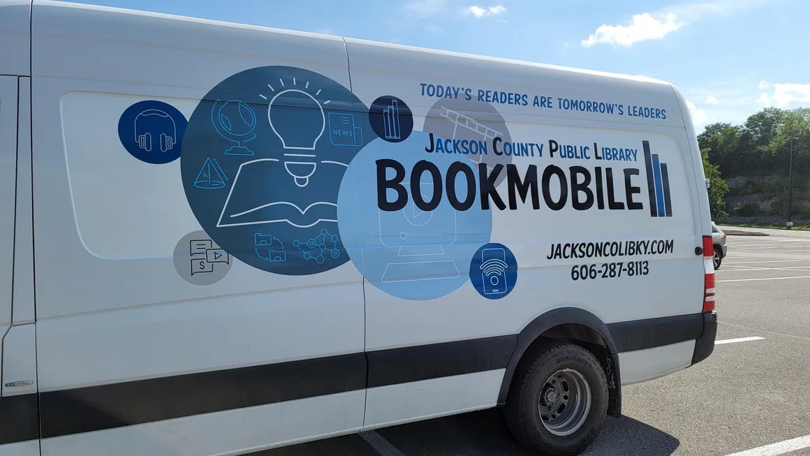 A library bookmobile van with educational graphics and contact information.