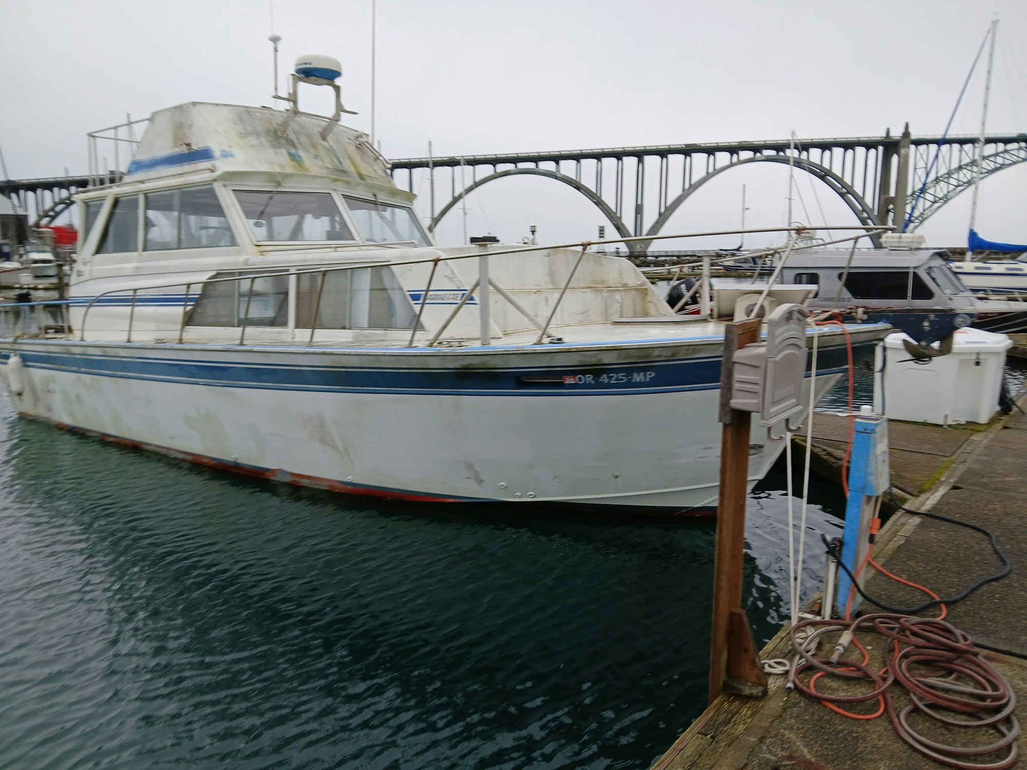 A weathered boat moored at a dock, with a bridge in the background.