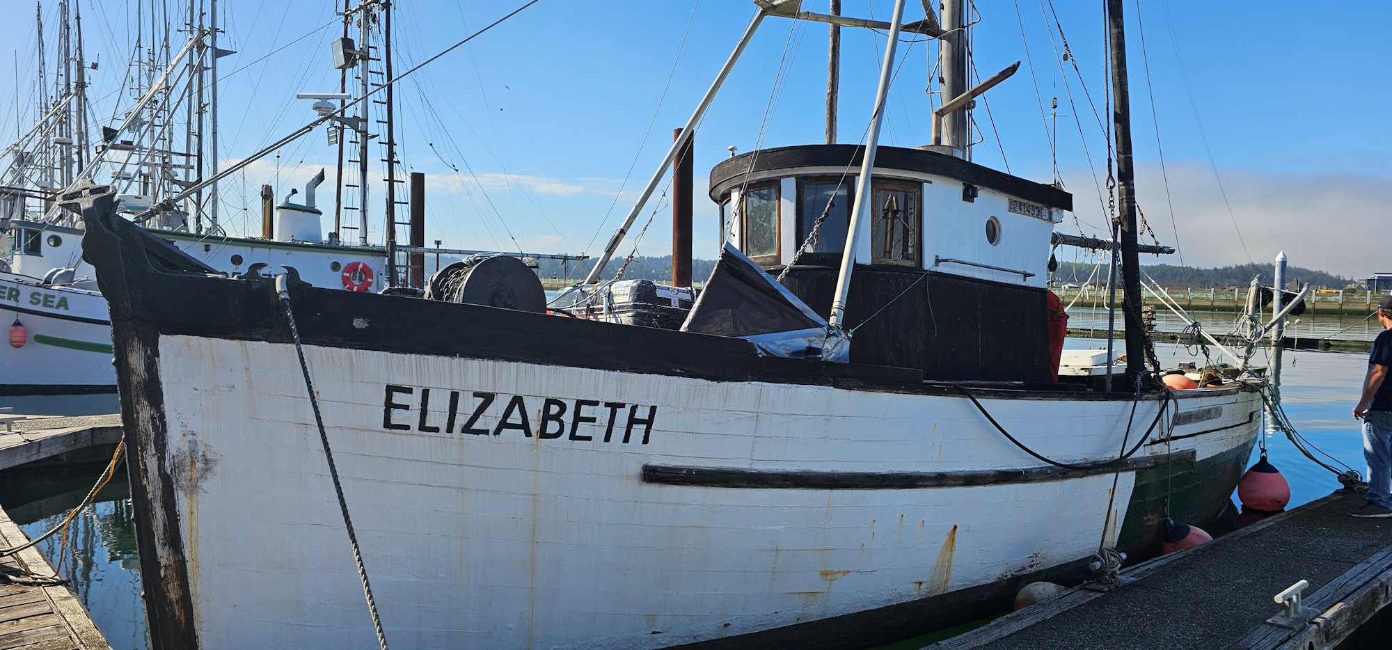 Fishing boats docked at a harbor; one named "ELIZABETH", clear skies, and a person on the dock.