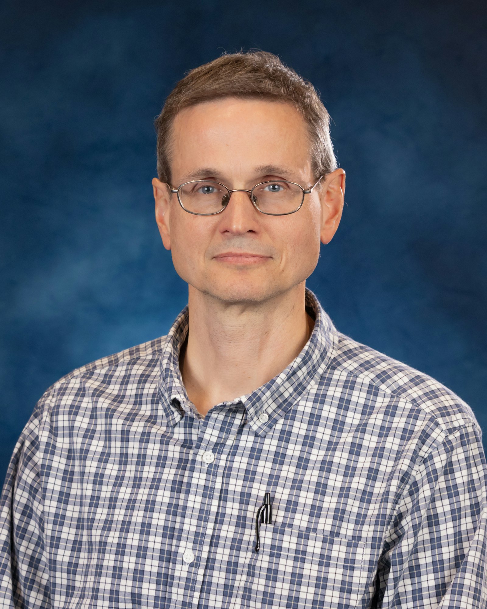 A man wearing glasses and a checkered shirt, against a blue background.