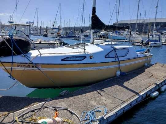 A small yellow and white sailboat docked at a marina with other boats in the background.