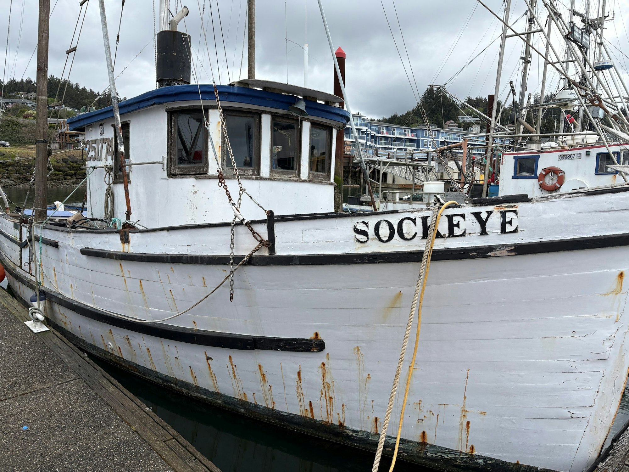 A weathered fishing boat named "Sockeye" docked at a marina, surrounded by other boats and buildings in the background.