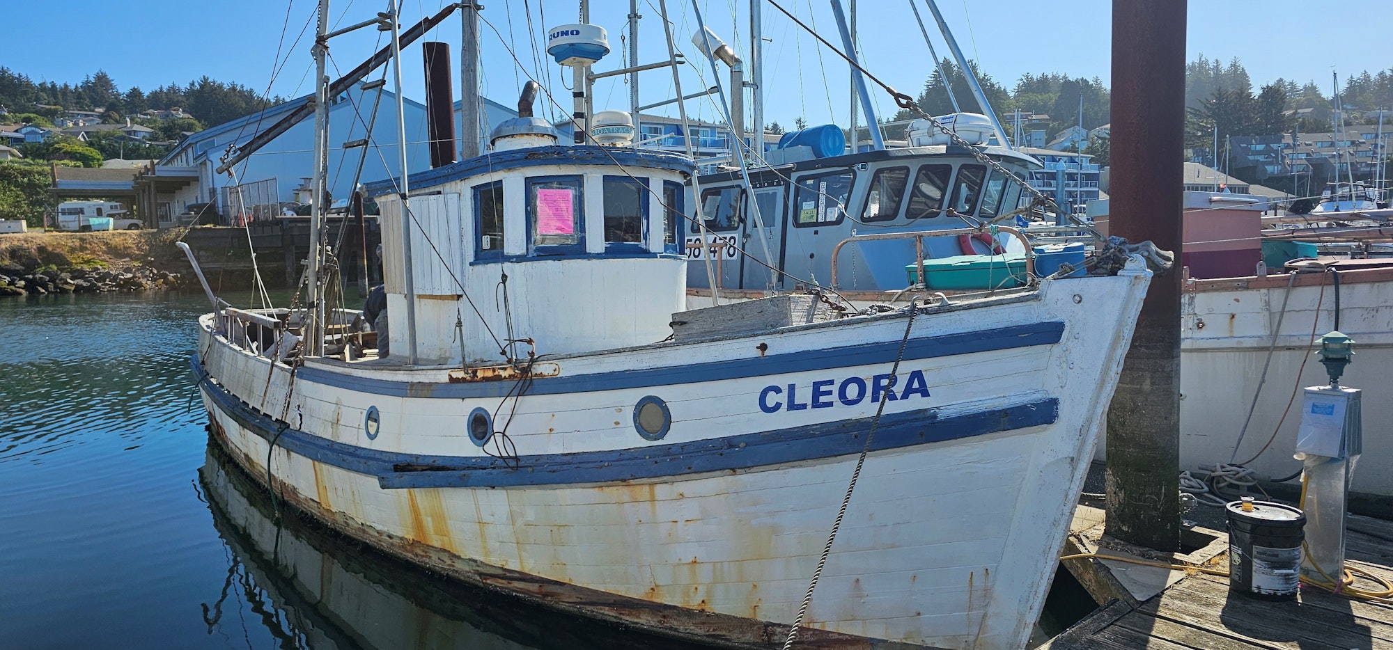A docked fishing boat named CLEORA with rustic charm, surrounded by various other boats and marine equipment.