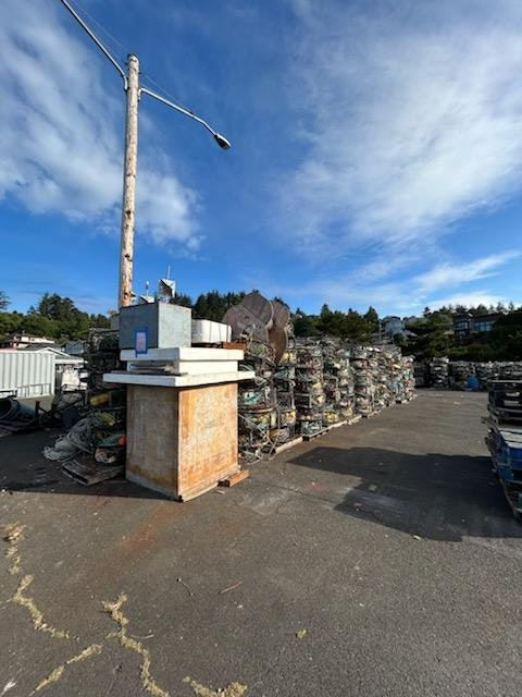 A lot filled with neatly stacked, weathered crab pots, a lamp post, and blue sky.