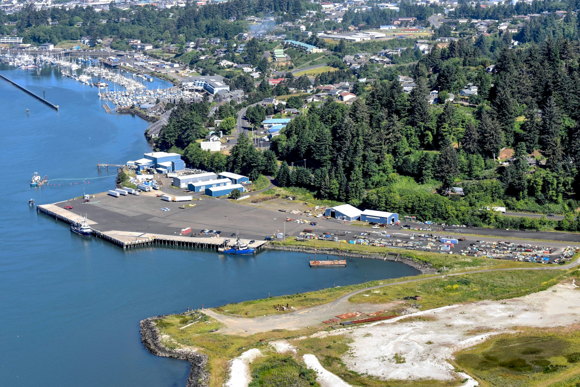 The image shows a waterfront area with boats, warehouses, and nearby greenery in a small coastal community.