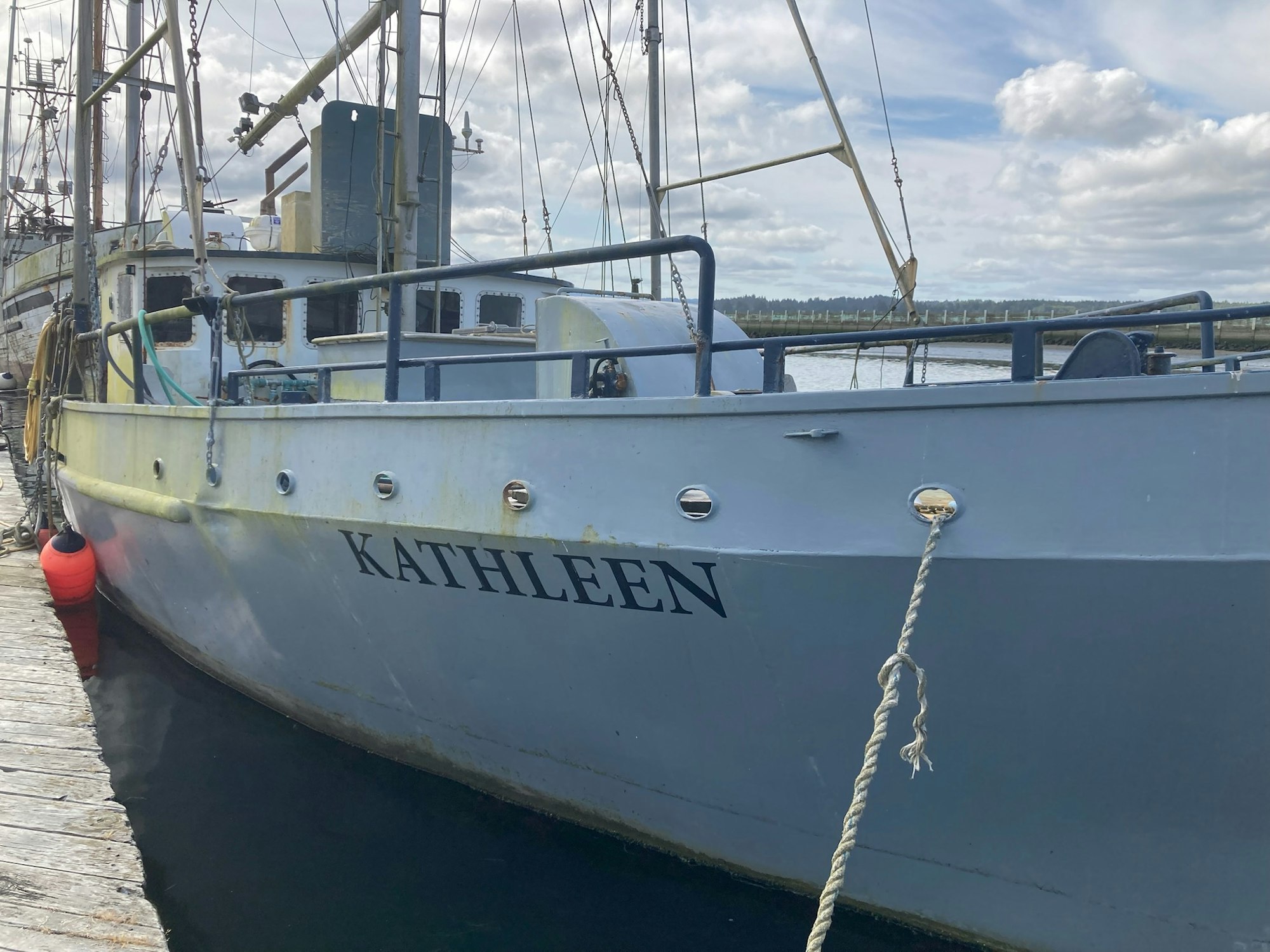 A docked boat named "KATHLEEN" tied to a wooden pier with a red buoy attached.