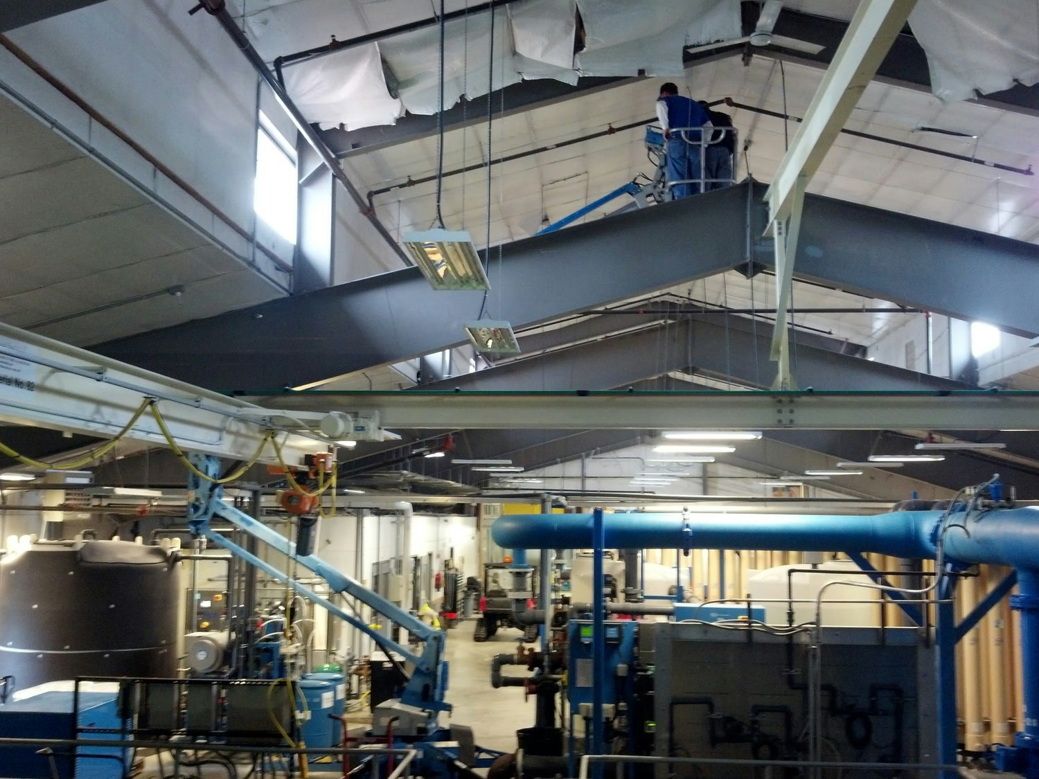 A spacious industrial facility with a worker on a lift near the ceiling and various machinery and equipment below.