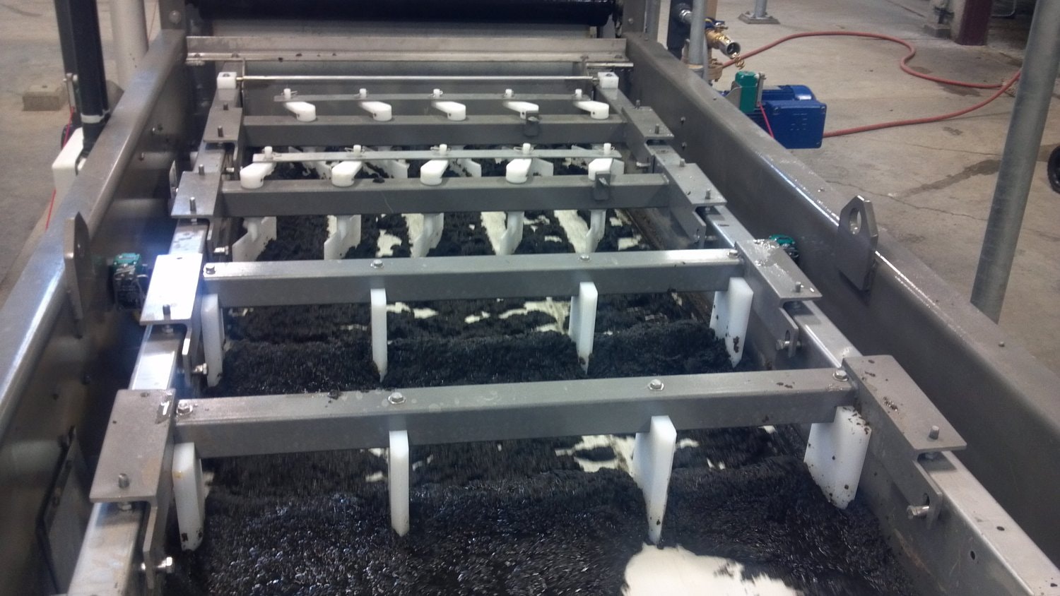 The image shows a mechanical system with metal and plastic components, possibly part of a processing or cleaning machine.