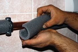 Hands installing foam insulation around a pipe.