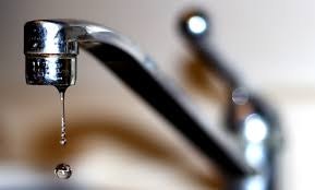 A close-up of a dripping faucet releasing a water droplet.