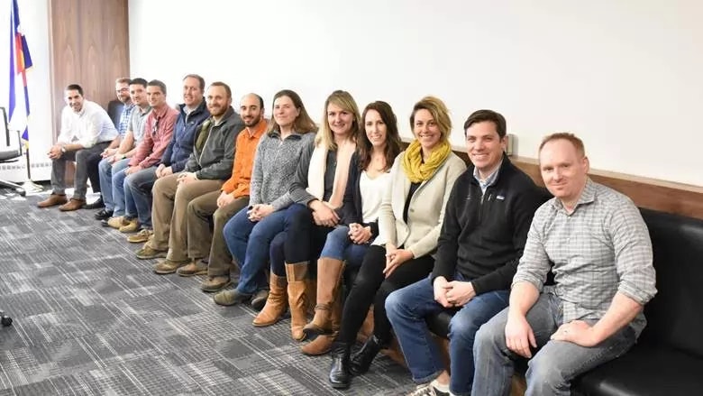 A group of people sitting in a row, smiling, in a casual indoor setting.