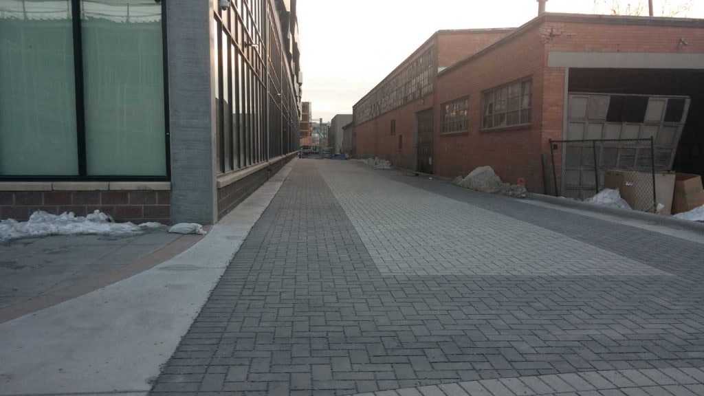 Urban alley with cobblestone pavement, modern building on the left, old brick building on the right, and patches of snow.