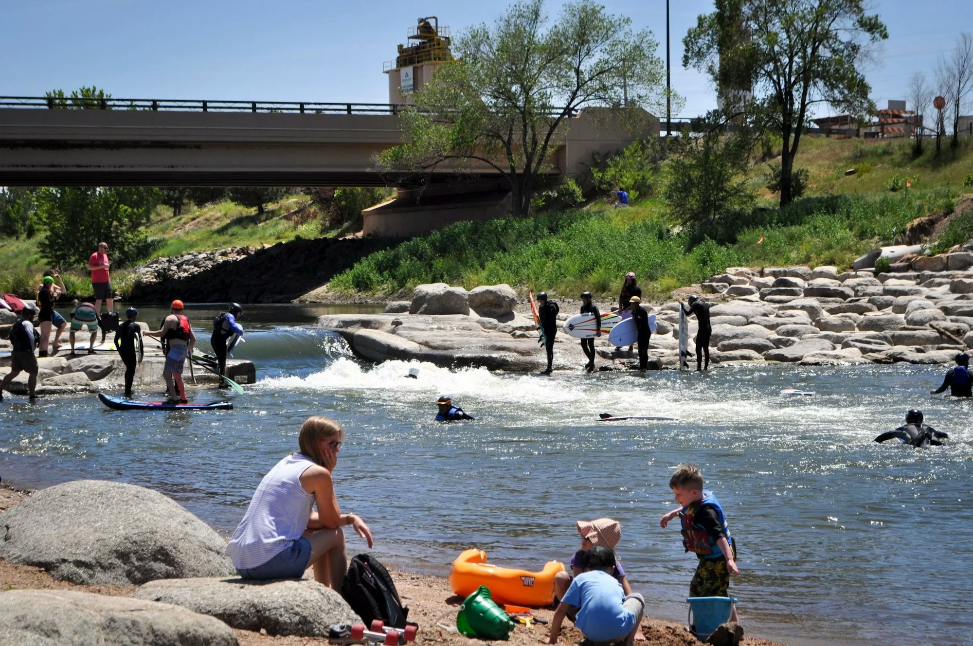 People enjoying outdoor activities on a sunny day at a riverbank with paddleboarding and relaxing.