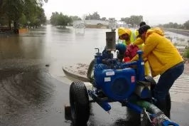 People using a pump near a flooded area.