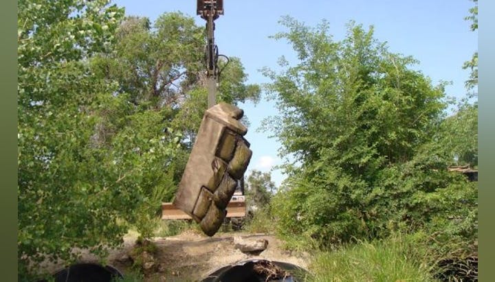 A mechanical excavator lifting a couch outdoors.