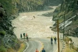 People by a swollen river next to a road, possibly observing flood conditions.
